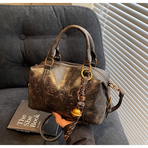 Vintage brown leather Boston bag with embossed lettering and bell charm on a velvet sofa