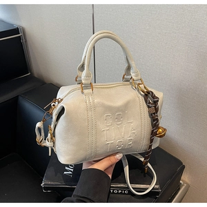 Close-up of beige leather Boston bag featuring Cultivator embossing and a golden bell charm