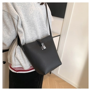 Detail of black lychee grain leather bucket bag with silver buckle worn by a model