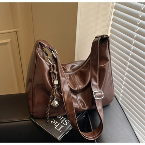 Detail of dark brown leather hobo bag featuring woven tassel and silver bell charm