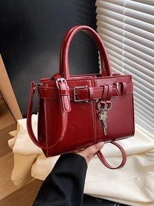 Glossy red leather handbag with silver buckle and key charm shown held by hand