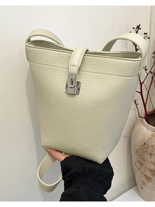 Minimalist beige litchi grain bucket bag with silver buckle held by hand in home setting