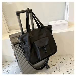 Detail of black nylon tote bag attached to a silver suitcase with metal buckle and strap