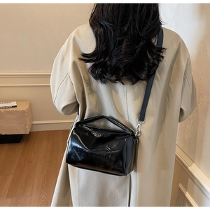 Detail of minimalist black patent leather shoulder bag with adjustable strap and embossed logo