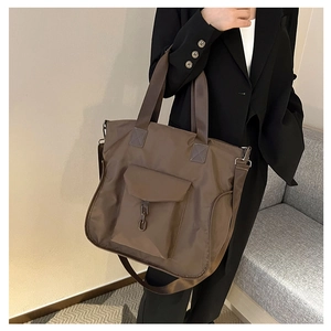 Detail of a dark brown nylon tote bag with metal chain pocket worn by a model in a suit