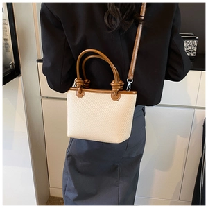 Détail du cabas en paille tissée avec poignées en cuir marron et nœuds décoratifs