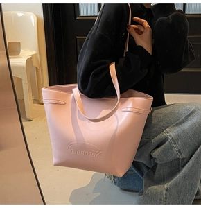 Detail of pink leather tote bag with embossed logo and slim shoulder strap on model