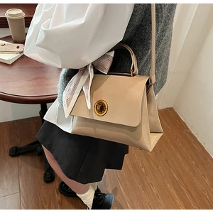 Close-up of beige handbag with gold metal lock and fashion scarf wrapped around handle