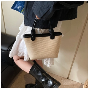 Détail d'un sac cabas tissé beige avec anses en cuir noir nouées et texture contrastée