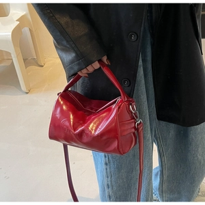 Macro view of a red glossy leather cylinder shoulder bag with embossed brand logo details