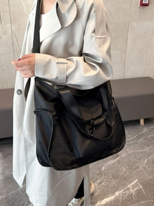 Large waterproof black nylon tote bag worn crossbody for casual commute and travel