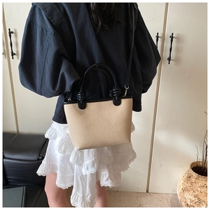 Détail du sac cabas en paille tissée avec anses noires montrant le style en bandoulière