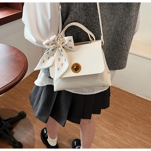 Detail of white faux leather crossbody bag with gold twist lock and polka dot scarf
