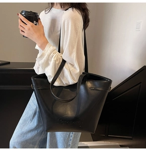 Detail of black leather tote bag with Nixononon engraving worn on model's shoulder