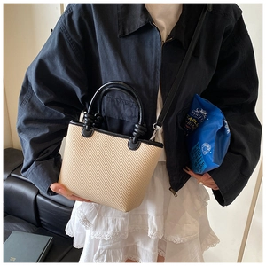 Gros plan sur les bordures en cuir contrasté et la paille tissée du sac seau