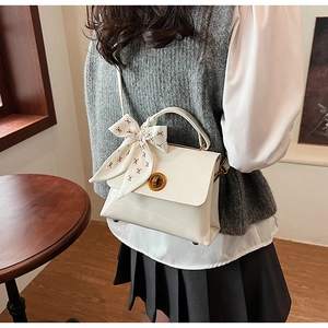 Detail of off-white leather satchel with golden lock and ribbon-wrapped handle