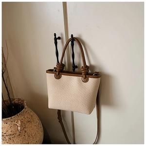 Détail d'un sac cabas en paille tressée avec anses en similicuir marun et nœuds décoratifs