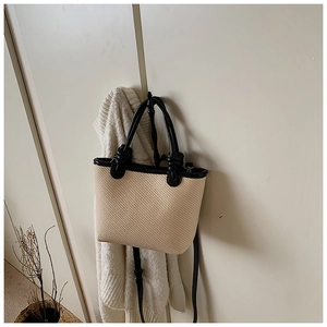 Détail du sac cabas en paille tissée avec bordure en cuir noir dans un cadre minimaliste