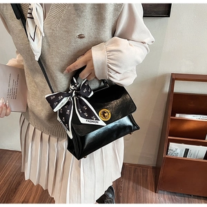 Detail of a black leather messenger bag with gold clasp and silk scarf handle decoration