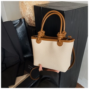 Détail d'un sac cabas tissé avec poignées en cuir marron et nœuds décoratifs