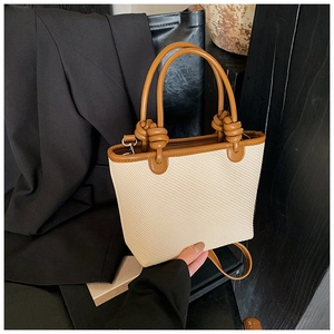 Détail du sac cabas tissé beige avec poignées en cuir marron et nœuds décoratifs
