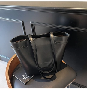 Close-up of black matte faux leather tote bag with oval embossed logo on leather chair