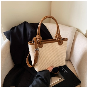 Détail d'un sac cabas en paille avec poignées en cuir marron nouées sur un canapé