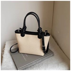 Détail du sac fourre-tout tissé beige avec bordure noire et poignée sur fond décoratif