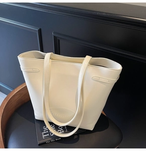 Detail view of large cream leather tote bag featuring debossed logo on black leather chair