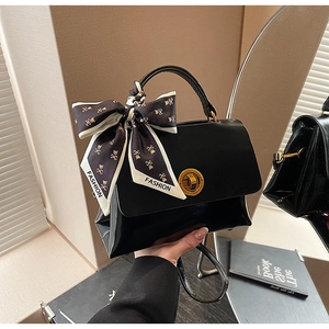 Detail of black handbag with gold rotary lock and stylish scarf on the handle