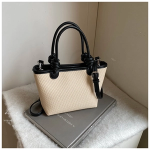 Détail d'un sac cabas tissé avec anses en cuir noir et accents décoratifs en nœud sphérique
