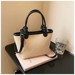 Détail d'un sac cabas beige en paille tressée avec bordure noire et anse à nœuds