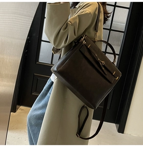 Detail of a dark brown matte leather backpack with gold buckle hardware on a beige trench coat