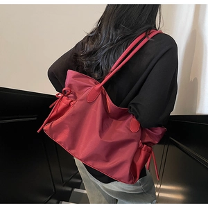 Détail du sac de voyage en nylon bordeaux avec poignées en cuir et nœuds latéraux décoratifs