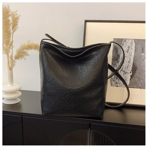 Détail du sac seau noir plissé avec logo embossé et fine bandoulière en cuir