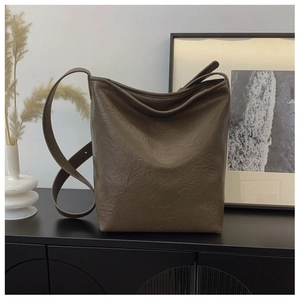 Détail d'un sac seau marron plissé avec large bandoulière sur surface noire