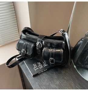 Detail einer schwarzen glänzenden Lackleder-Schultertasche mit zwei Metallschnallentaschen