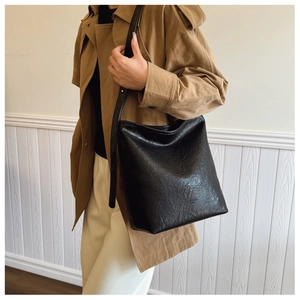 Sac à bandoulière noir plissé porté par un mannequin avec un trench-coat classique