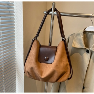 Detail of a brown suede tote bag with leather strap and decorative buckle in warm light