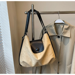Close-up of beige suede tote bag with black faux leather strap on metal display rack