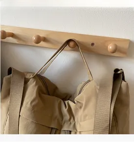 Detail of khaki nylon tote bag hanging on wooden hooks with durable shoulder straps