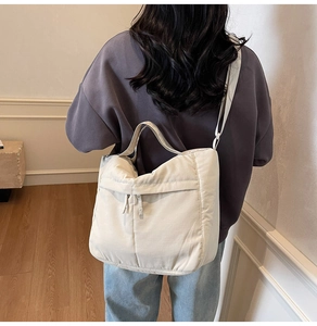 Detail of light beige quilted nylon tote bag with front zipper pocket shown on model