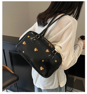Close-up of black glossy underarm bag with gold heart studs and twin shoulder straps