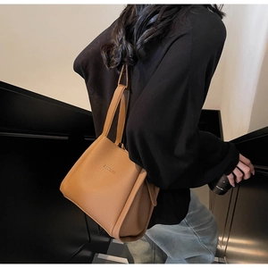 Brown litchi leather bucket bag with top handles shown on model in urban setting