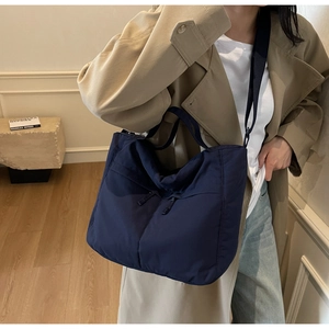 Detail of navy blue nylon tote bag with pocket worn with a khaki trench coat