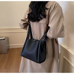 Detail of black lychee grain leather bucket bag with wide handle worn over a trench coat
