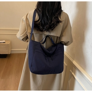 Detail of dark blue nylon tote bag with front zipper pockets worn by a model in a trench coat