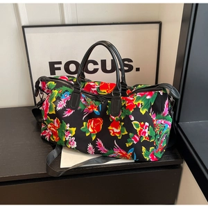 Detail of floral duffel bag with black leather handles and adjustable nylon shoulder strap