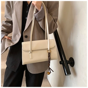 Detail of a beige rectangular flap shoulder bag with beaded charm and twin slim straps