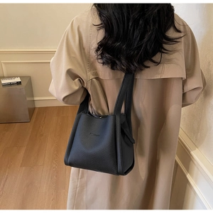 Detail of black pebbled leather bucket bag with embossed logo on a khaki trench coat